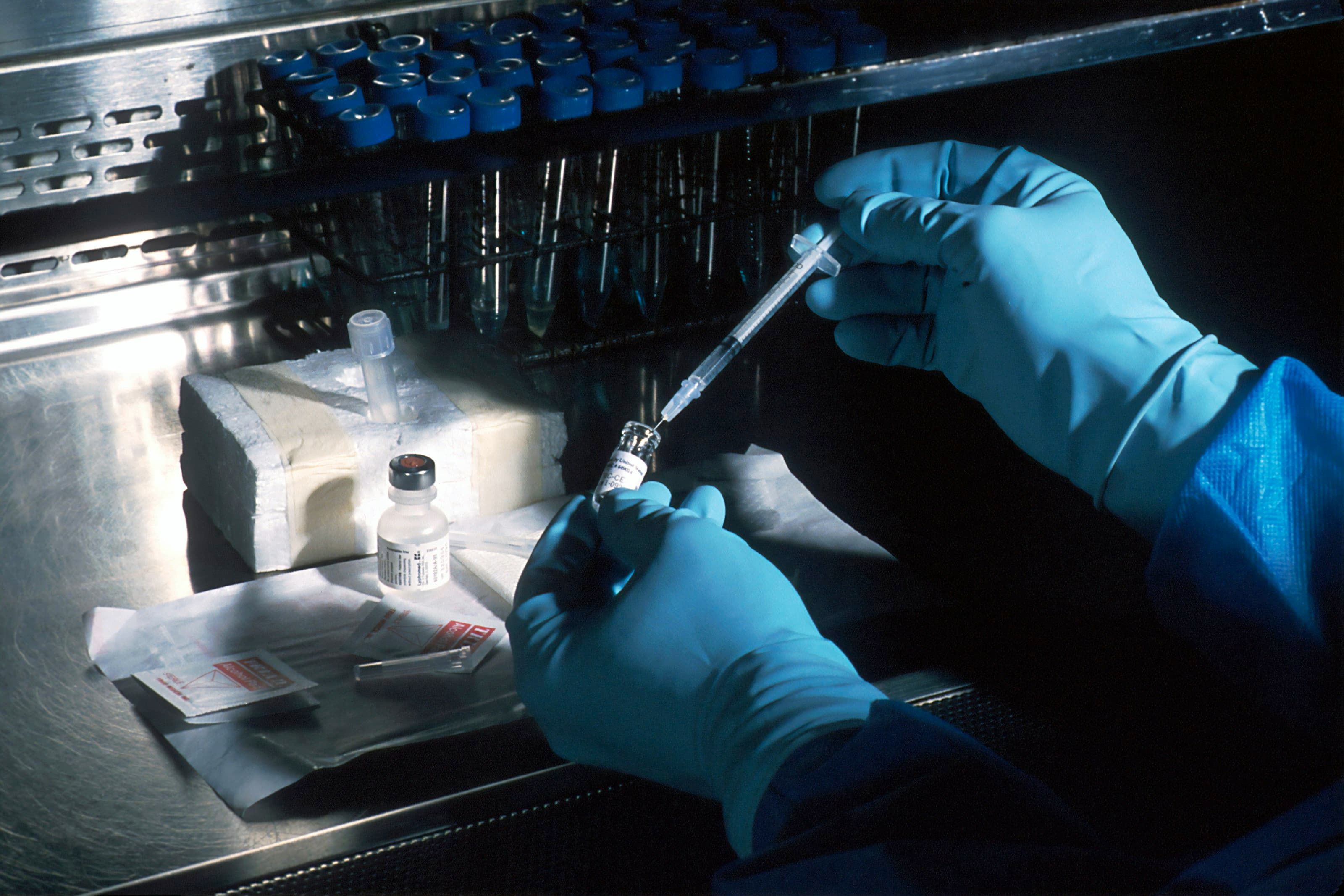 Gloved hands drawing a dose from a vial in a laboratory